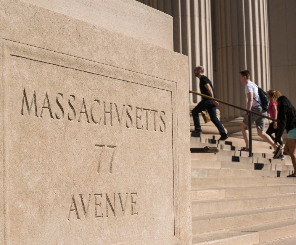 Photo of stone block depicting 77 Massachusetts Avenue sign. People walking up stone steps in the background. 