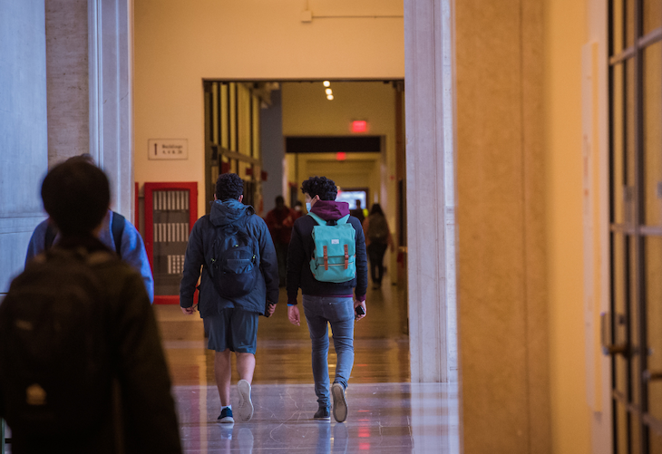 Photo of students walking away from camera down the Infinite Corridor, turned as if talking to each other. 